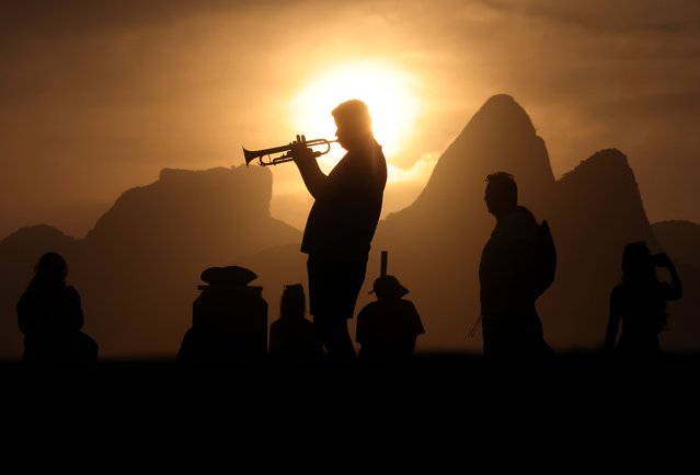 A street performer plays the trumpet on the boardwalk at Arpoador in Rio De Janeiro on October 6, 2025, as hundreds gather to watch the sunset in front of the silhouette of the iconic Two Brothers mountains. (Photo by Bob Karp/ZUMA Press Wire/Rex Features/Shutterstock)