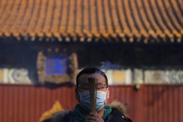 A man wearing a face mask to help curb the spread of the coronavirus holds incense offers prayers on the first day of the New Year at Yonghegong Lama Temple in Beijing, Friday, January 1, 2021. President Xi Jinping said in a New Year address that China has made major progress in developing its economy and eradicating rural poverty over the past year despite the coronavirus pandemic. (Photo by Andy Wong/AP Photo)