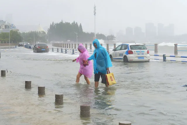 Local residents walk on the flooded banks along the seacoast caused by Typhoon Ampil, the tenth typhoon of the year, in Qingdao city, east China's Shandong province on July 23, 2018. China's national observatory on Sunday evening renewed a yellow alert for rain, saying that many places including Guangxi, Guangdong, Hainan, Jiangsu and Shandong will be hit by heavy rain. China has a four-tier color-coded weather warning system, with red representing the most severe weather, followed by orange, yellow, and blue. (Photo by Imaginechina/Rex Features/Shutterstock)