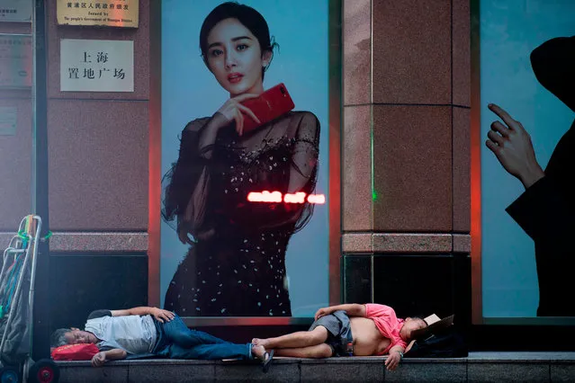 In this photo taken shortly after midnight on August 9, 2018, a man sleeps in front of a shopping mall along Nanjing East Road, a popular pedestrian street filled with shoppers and tourists during the day, to escape the heat of residential apartments in Shanghai. Normally bustling Nanjing East Road has turned into an open- air slumber party on recent nights as local residents try to beat the heat of their cramped nearby homes by sleeping outside on benches or directly on the pavement. Many homes in some of Shanghai' s low- rise older neighbourhoods lack air conditioning, while residents that do have it will often seek ways to keep electricity bills from skyrocketing during summer. (Photo by Johannes Eisele/AFP Photo)